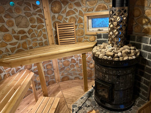 A Volcano model masonry sauna heater with amphibolite black stone cladding, installed in a unique cordwood masonry sauna with cedar benches.