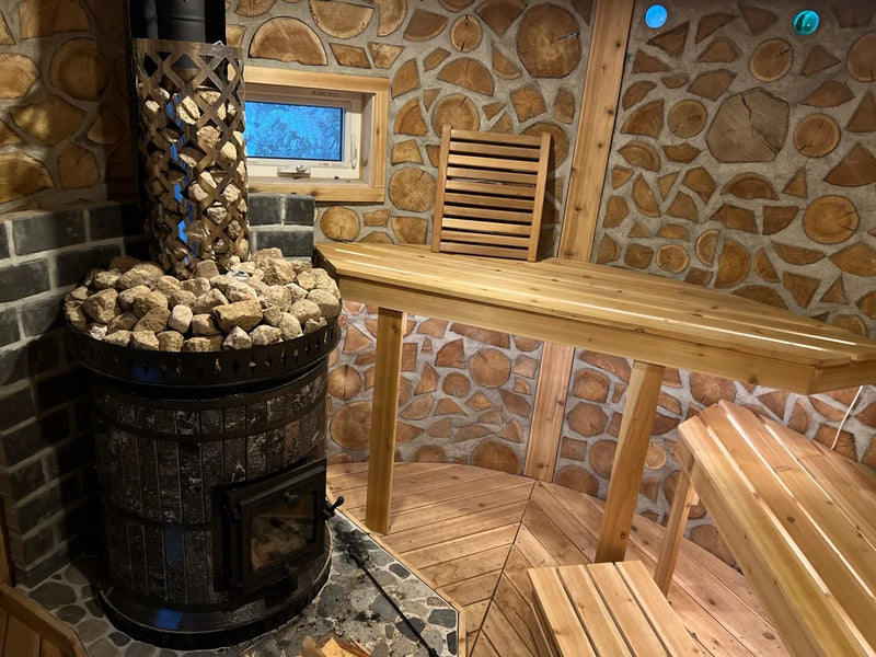 A Volcano model masonry sauna heater with amphibolite black stone cladding, installed in a unique cordwood masonry sauna with cedar benches.