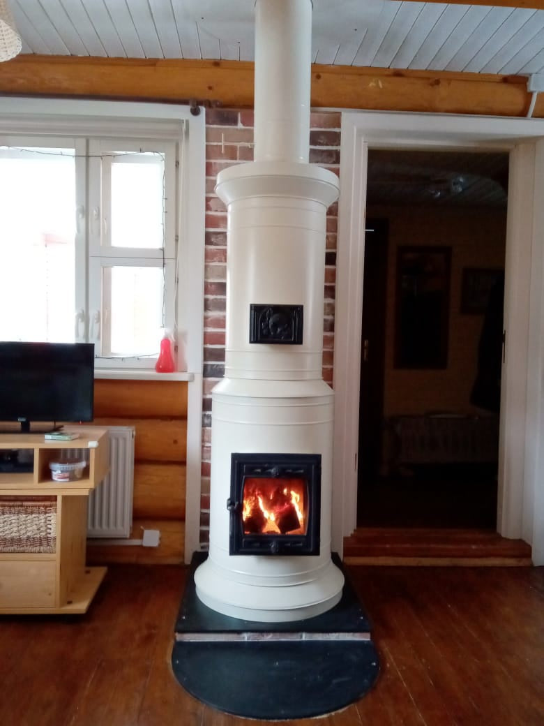 A smooth white Venice masonry heater acting as the focal point in a cottage living room with light blue wood-paneled walls.