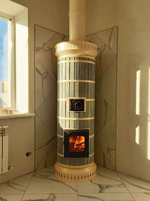 A blue soapstone Tundra masonry heater installed in a sunlit corner, backed by a custom white marble tile heat shield.