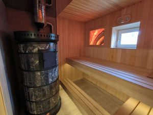 black ampholite masonry sauna heater installed in a wooden sauna with backlit Himalayan salt panel and tiered benches