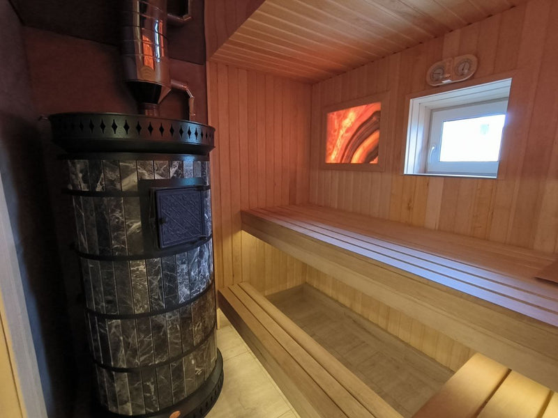 black ampholite masonry sauna heater installed in a wooden sauna with backlit Himalayan salt panel and tiered benches
