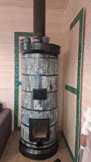 A Siberia green serpentine masonry heater featuring custom matching green stone trim on the wall behind the unit.