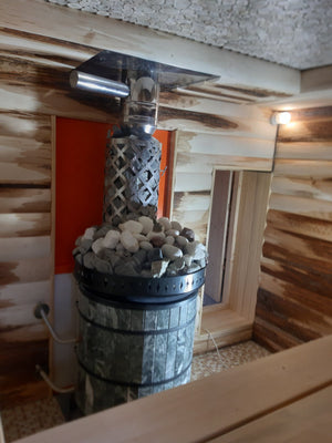 Close up of diamond-pattern stainless steel rock basket on green serpentine stone sauna heater filled with white stones