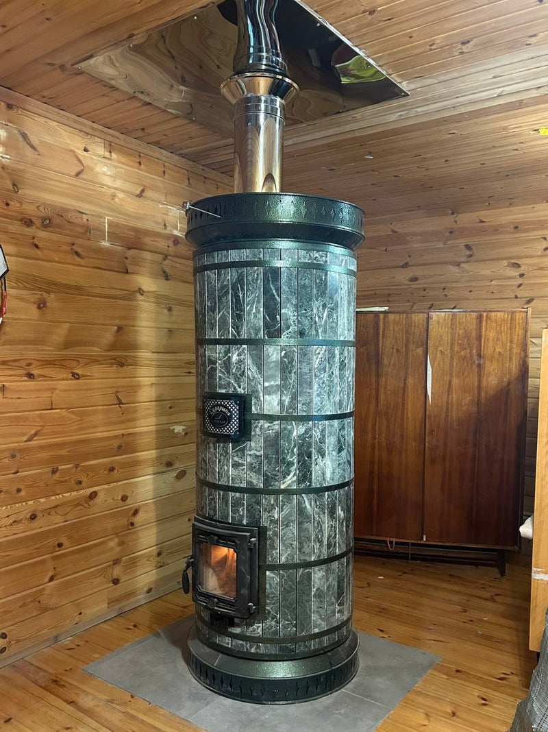 A siberia serpentine stone masonry heater with glass firebox door active in an off-grid workshop or cabin.