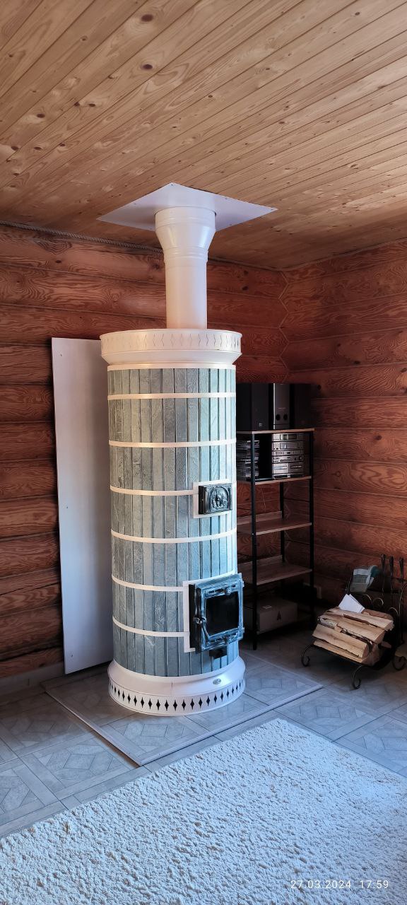 A recently assembled DIY Siberia masonry heater kit standing on a base in a log home under construction, showing the unit before final cleaning.