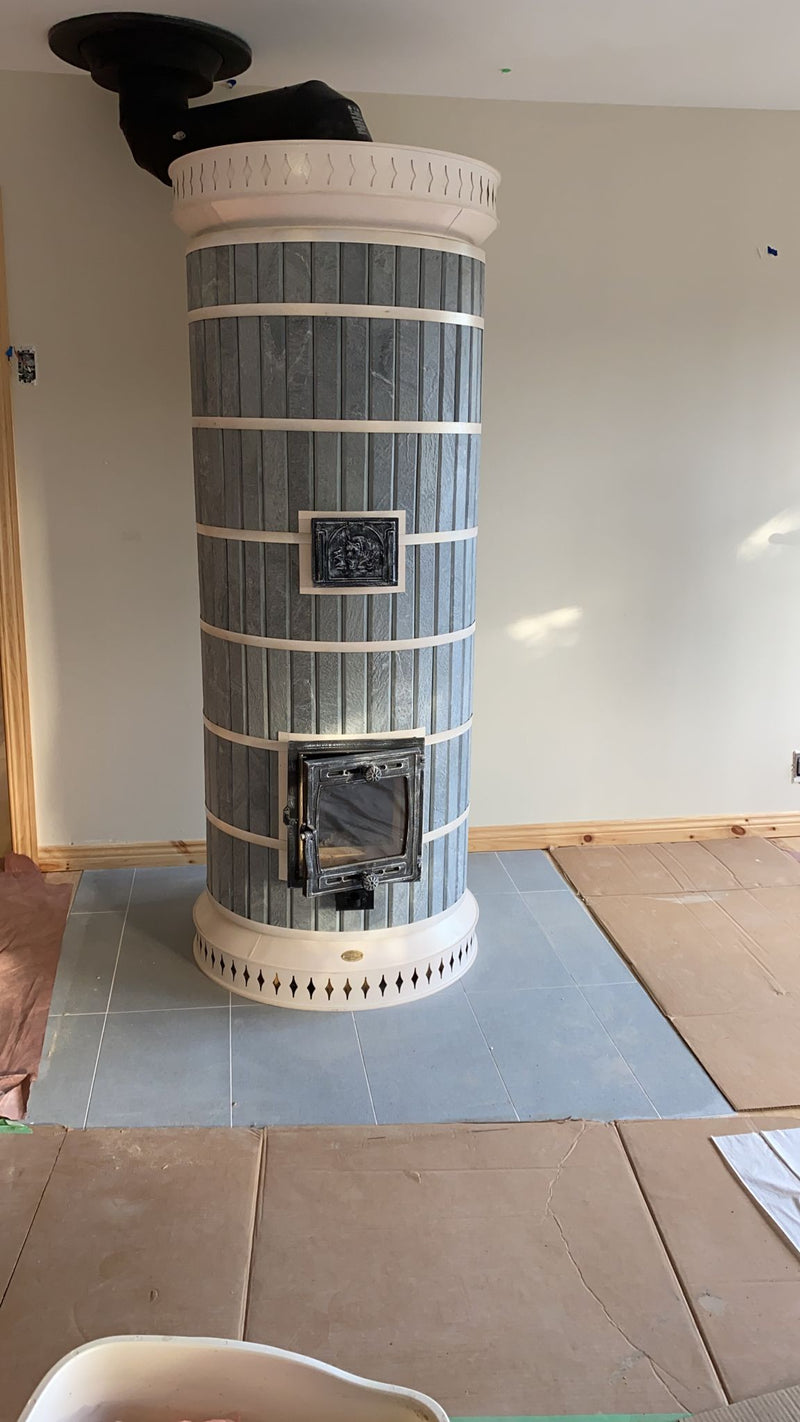 A newly installed DIY Siberia soapstone masonry heater on a grey tile hearth, showing the completed assembly before the room is furnished.