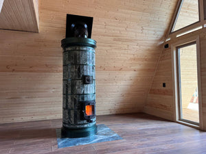 High-efficiency green serpentine Siberia masonry heater kit installed in a wooden A-frame cabin, providing radiant thermal mass heating for high ceilings.