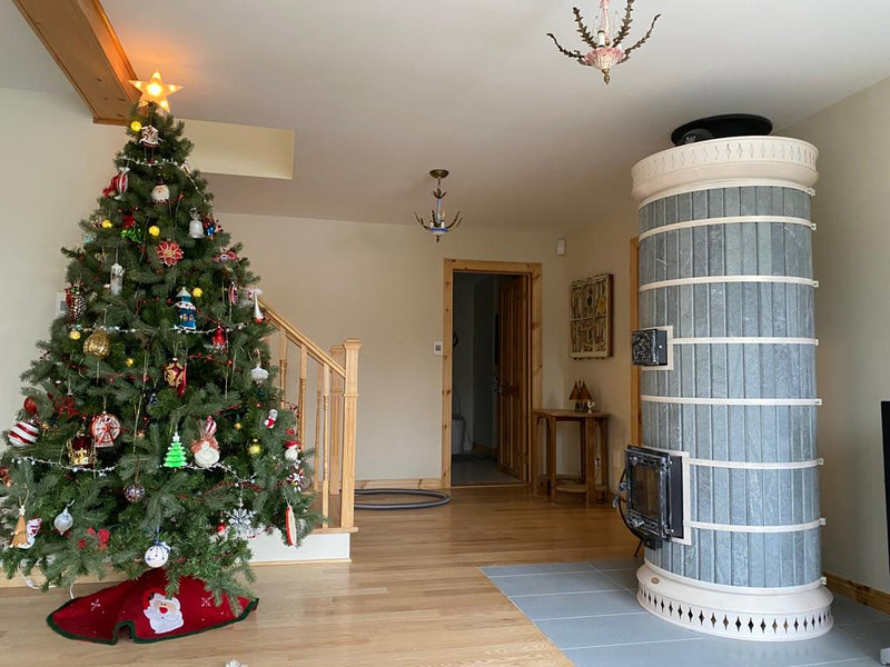 A finished DIY Siberia  masonry heater kit with grey soapstone cladding installed in a home with wooden floors and holiday decor.