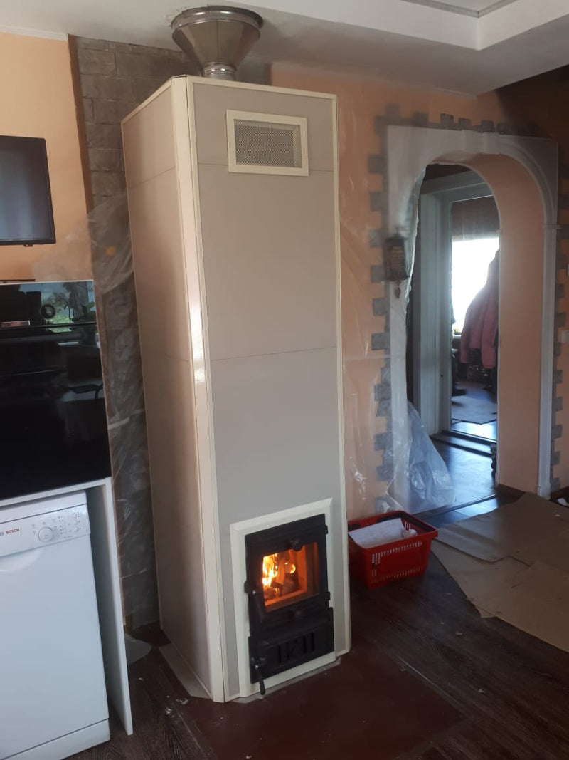 A Mont-Tremblant masonry heater with a smooth beige panel finish, installed in a home featuring an arched doorway and modern appliances