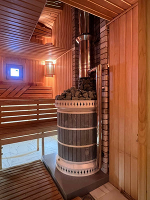 Side view of wood fired blue soapstone sauna masonry eater showing safe installation distances from wooden benches and stainless steel chimney connection