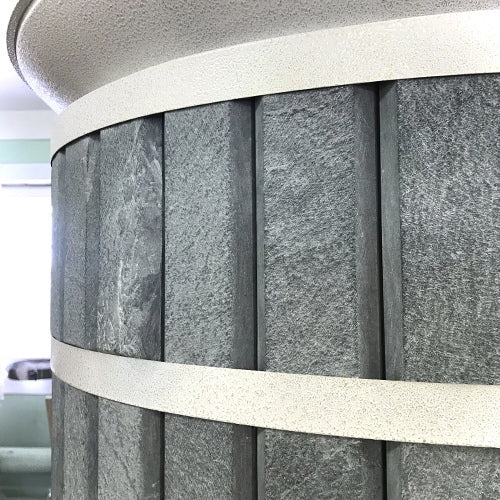 Close-up detail of the natural grey soapstone cladding on a Siberia masonry heater, showing the vertical stone grain and white trim rings.