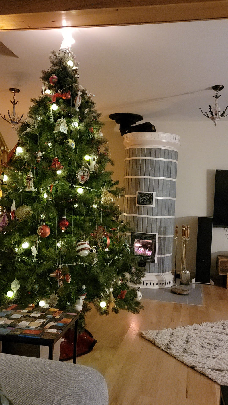 A Siberia soapstone  masonry heater serves as the cozy centerpiece of a rustic living room beside a decorated Christmas tree.