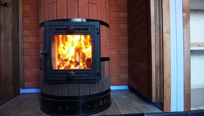 Close-up view of the cast iron glass door on a red brick Tundra masonry heater, showing the clean-burning wood fire inside.