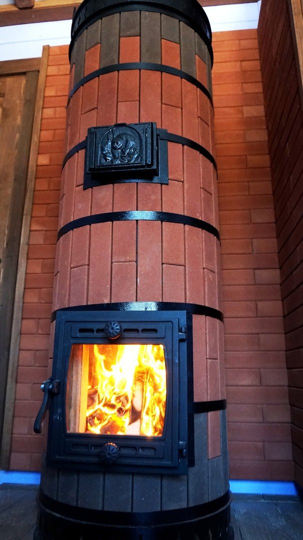 Close-up of a Tundra model masonry heater featuring a unique round red brick design with black steel banding and a cast iron firebox door.