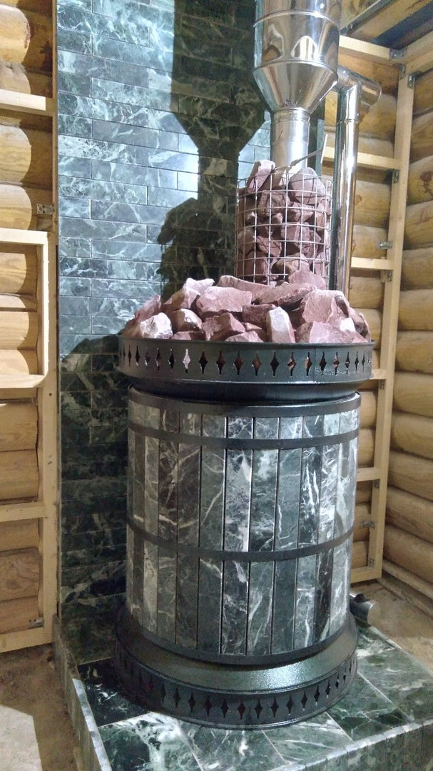 Green serpentine masonry sauna heater installed against a matching green stone heat shield wall in a log cabin sauna