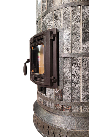 Side profile close-up of the Siberia Amphibolite masonry heater, showing the curved black stone cladding, black steel banding, and heavy-duty cast iron door hinges.