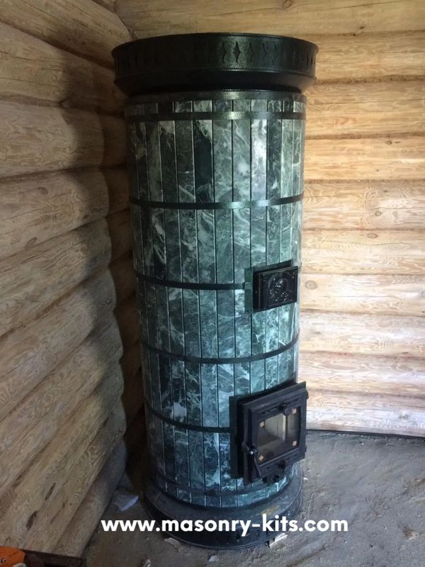 A rustic log cabin interior featuring a floor-to-ceiling Siberia green serpentine stone masonry heater.