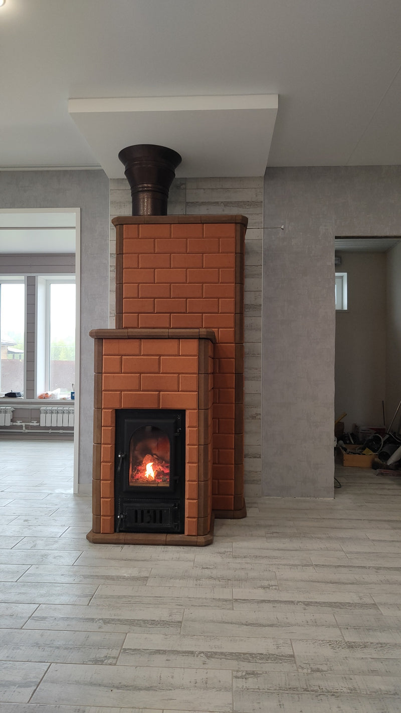 A finished Lapland red brick masonry heater installed in a modern living room, showing the offset chimney structure and cast iron firebox.