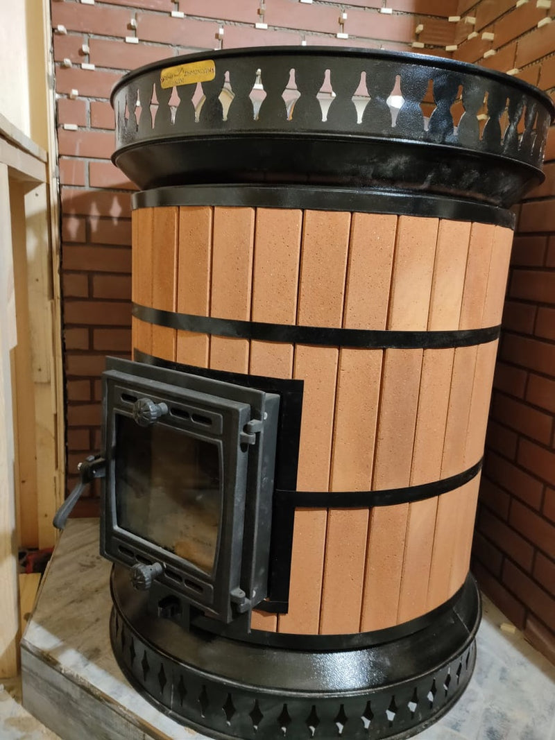 A finished Volcano model masonry sauna heater featuring red brick thermal mass cladding, black steel banding, and a top basket for sauna stones.