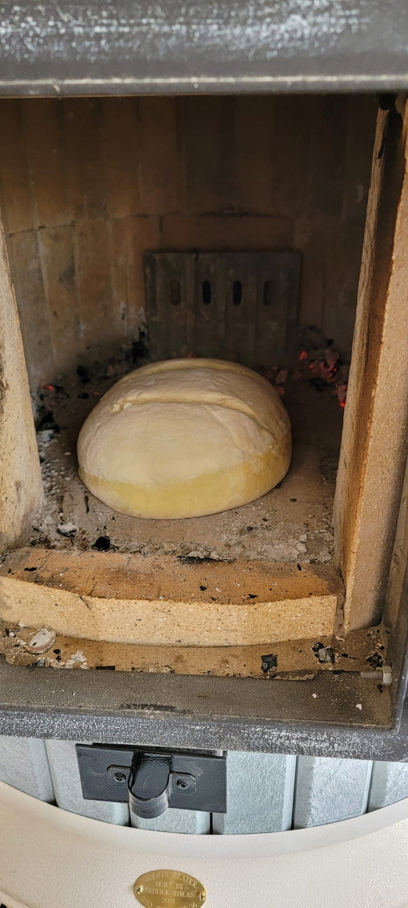 A loaf of sourdough bread rising and baking directly on the hot refractory bricks inside a Siberia masonry heater after the fire has died down.